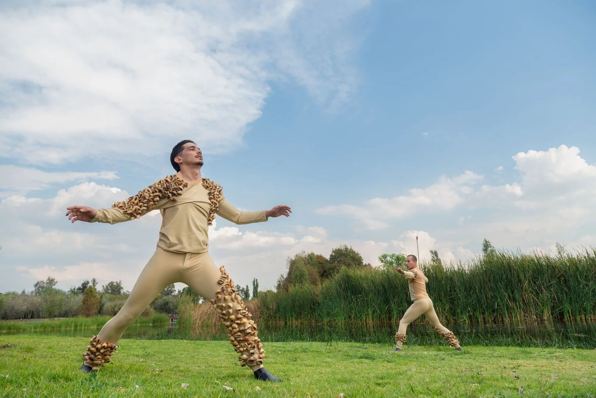 Performers in seed-covered costumes on the water's edge, Aki Aora 2025