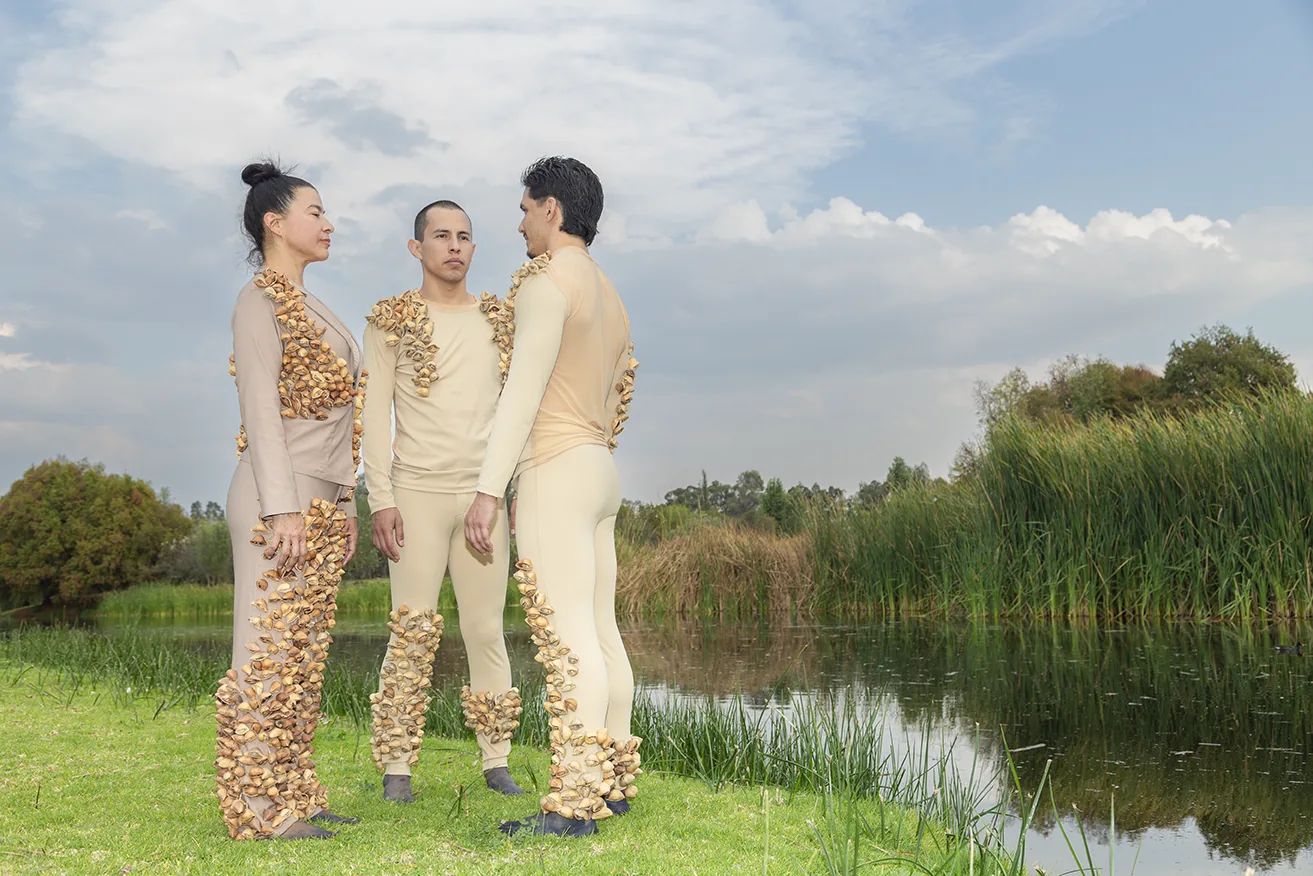 Performers in seed-covered costumes by the water, Aki Aora 2025